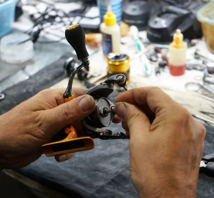Hands servicing a spinning reel on a workshop bench